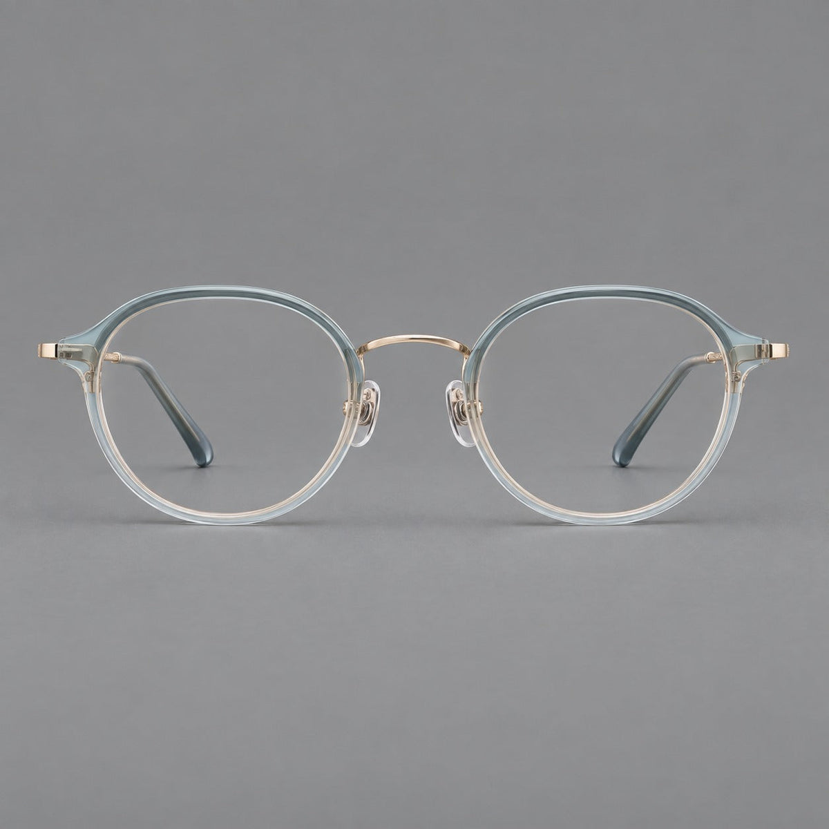 Softly rounded eyeglasses in acetate and titanium with a curved bridge and engraved temples in Ice Blue Gray / Gold, front view