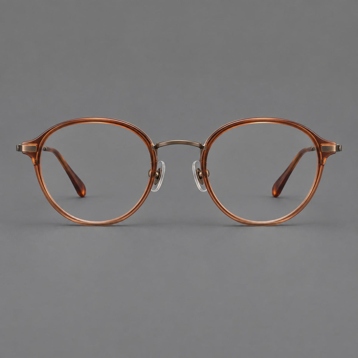 Softly rounded eyeglasses in acetate and titanium with a curved bridge and engraved temples in Tea Brown / Antique Bronze, front view