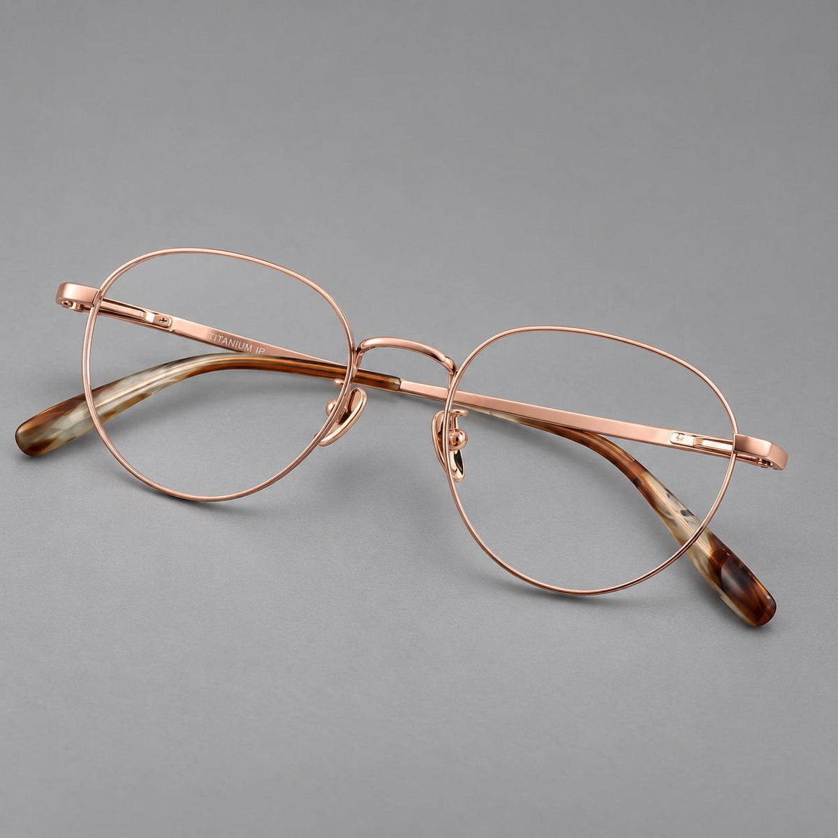 Classic round titanium glasses with broad flat temples and inset hinge details in Rose Gold, three quarter view