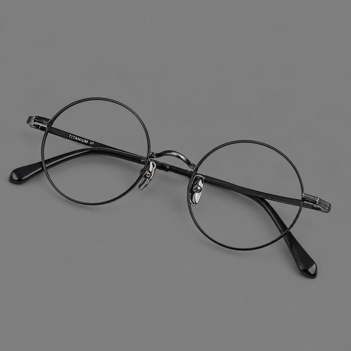 Compact circular titanium glasses with a curved bridge and wavy engraved temples in Black, three quarter view