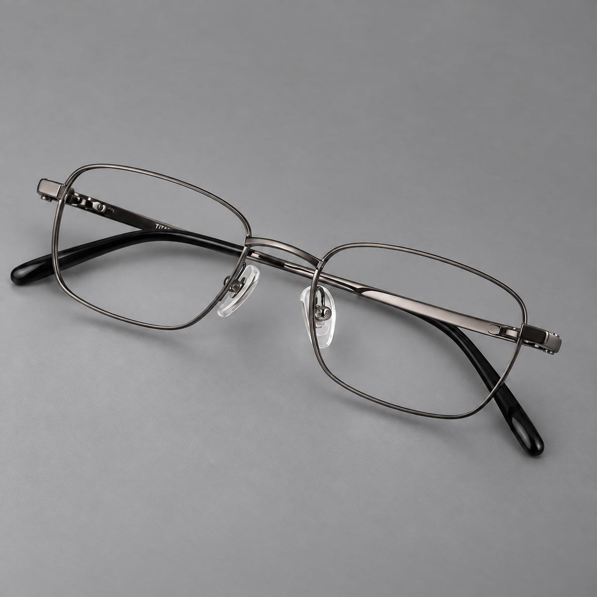 Shallow rectangular titanium glasses with a broad bridge and stepped temple joins in Gunmetal, three quarter view