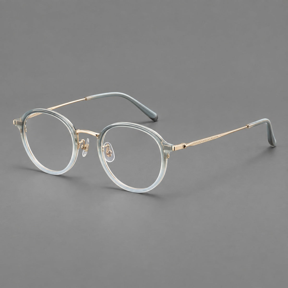 Softly rounded eyeglasses in acetate and titanium with a curved bridge and engraved temples in Ice Blue Gray / Gold, three quarter view