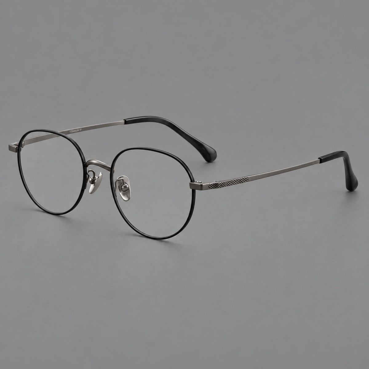 Compact round titanium glasses with an arched bridge and textured temple accents in Black and Gunmetal, three quarter view