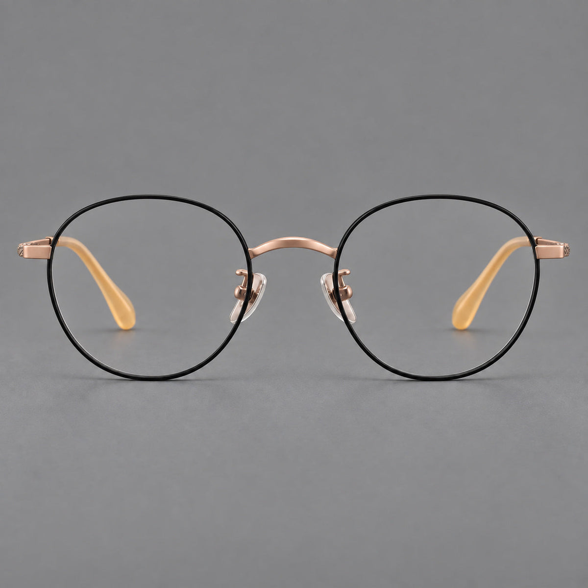 Compact round titanium glasses with an arched bridge and textured temple accents in Black and Rose Gold, front view