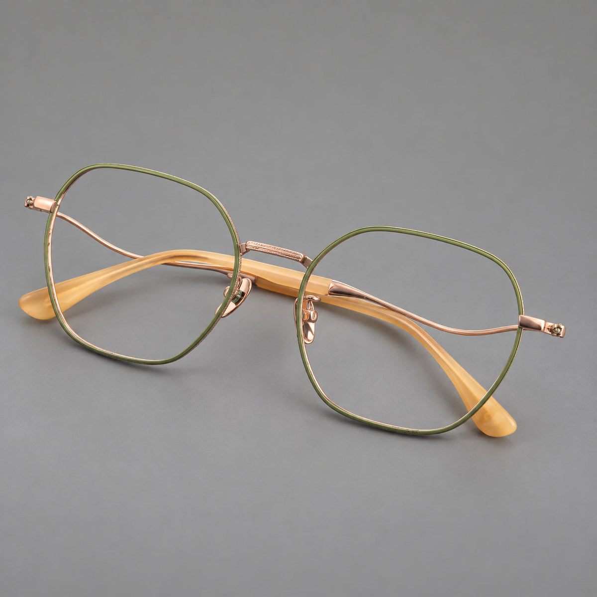 Geometric titanium glasses with engraved rim edges and curved temple joins in Green and Rose Gold, three quarter view