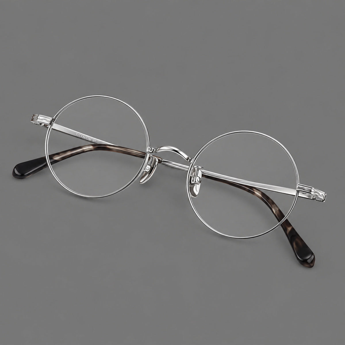 Compact circular titanium glasses with a curved bridge and wavy engraved temples in Silver, three quarter view