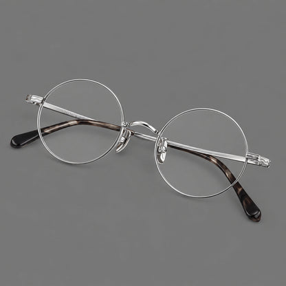 Compact circular titanium glasses with a curved bridge and wavy engraved temples in Silver, three quarter view lens detail