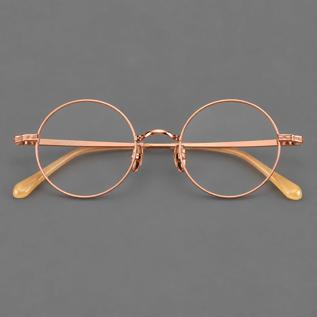 Compact circular titanium glasses with a curved bridge and wavy engraved temples in Rose Gold, front view