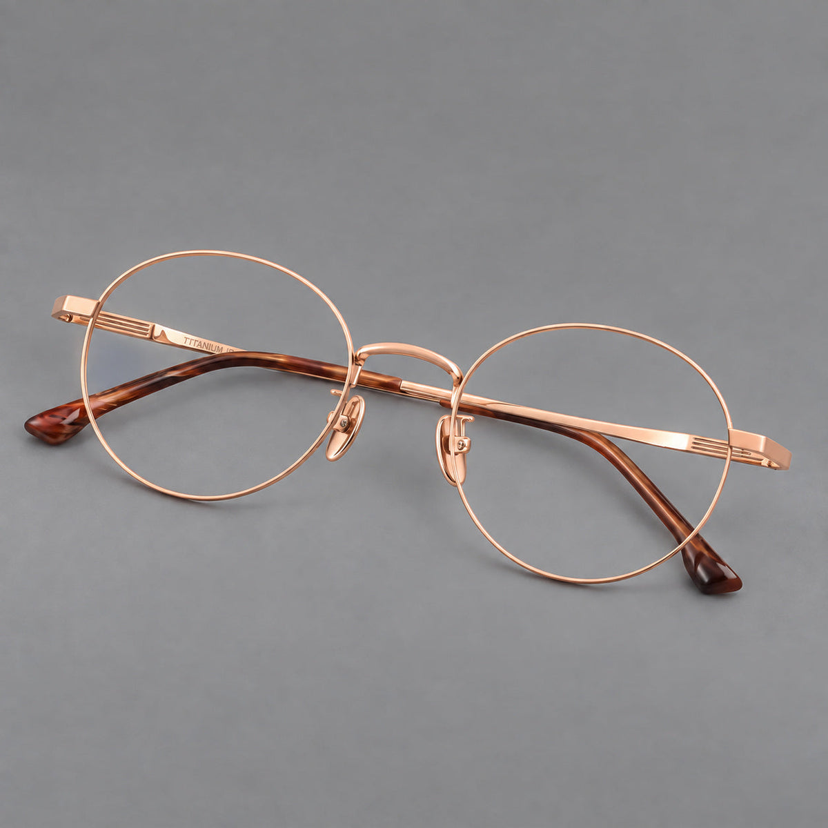 Classic circular titanium glasses with a raised bridge and lined temple accents in Rose Gold, three quarter view