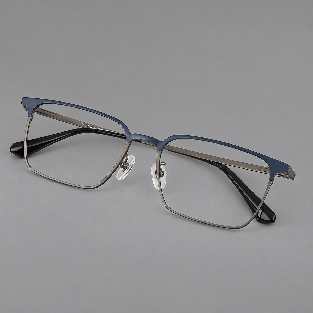 Bold rectangular titanium glasses with strong upper corners and flat metal temples in Blue and Gunmetal, three quarter view