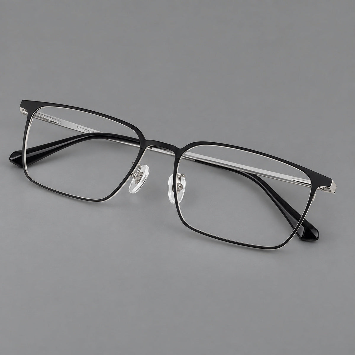 Bold rectangular titanium glasses with strong upper corners and flat metal temples in Black and Silver, three quarter view